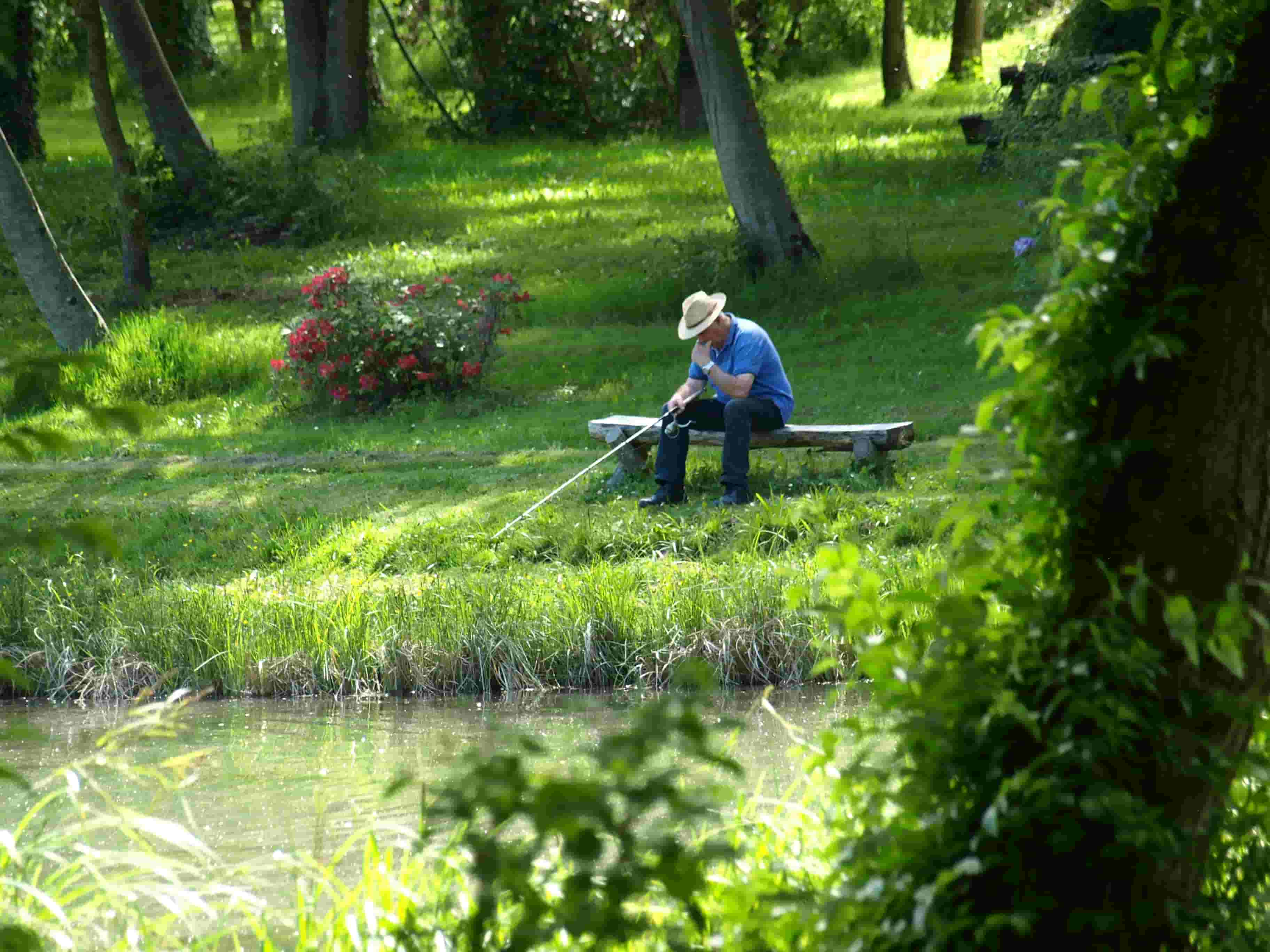 Pêcheur pensif regardant la surface de l'eau d'un étang assis sur son banc